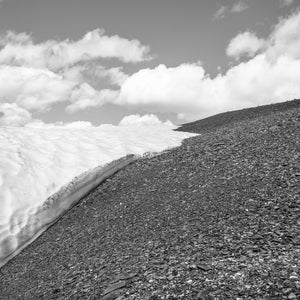 Bright snow meets a dark rocky mountain slope beneath clouds in the Bugaboos.