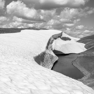 Sculpted snowbanks border dark meltwater beneath clouds in the Bugaboo Mountains.