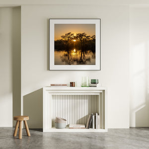 Cypress silhouettes surround a glowing sunset and its bright reflection on the water.