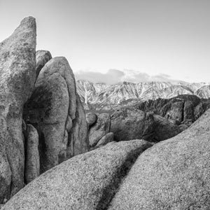 Rounded foreground boulders lead toward a snow-covered mountain ridge in California.