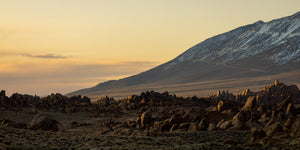 A pale golden sky contrasts with dark rocks and a broad mountain ridge in California.