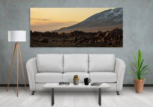 Panoramic landscape photograph of rugged foreground stones and snowy mountain slopes at sunset.