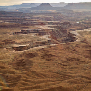 Terraced desert cliffs and winding canyon formations stretch toward distant flat topped mesas.