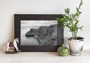 The Cliffs of Moher curve above quiet water beneath bands of cloud in black and white.