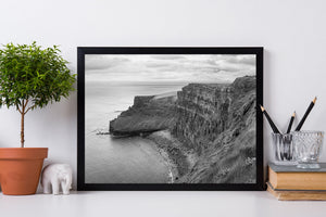 Rugged Irish sea cliffs show textured rock faces below a grassy edge and grey sky.