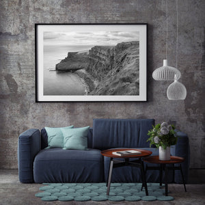 Monochrome Atlantic coast photograph with steep cliffs and a pale line of waves along the rocks.