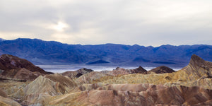 A panoramic desert photograph shows pale cream and rose hills before dark blue mountain ranges.