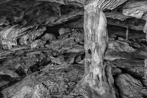 A pale stone column connects the floor and ceiling among rugged cave formations.