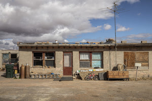 Colour photograph of a low desert building with rough siding and a tall rooftop antenna.