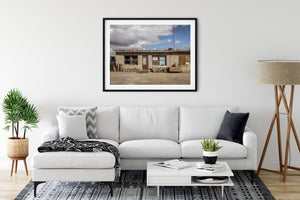 An old Arizona gas station home stands on bare ground beneath dark clouds and blue sky.
