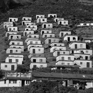 Small white houses climb a dark slope in a repeating pattern of walls and doorways.