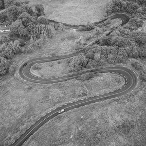 A narrow road curves through multiple hairpin bends across a textured Irish hillside.