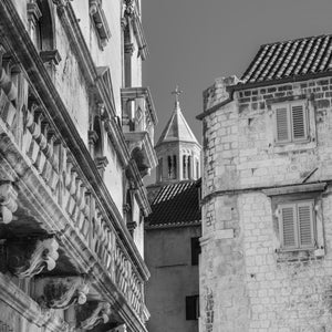 A carved stone balcony faces a rounded old building beneath a tiled roof in Croatia.