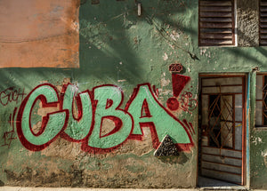 Bold red and pale lettering contrasts with peeling green paint on an old Cuban facade.