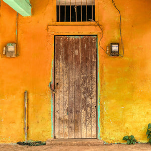 An old Cuban doorway contrasts dark wooden boards with warm orange and yellow plaster.