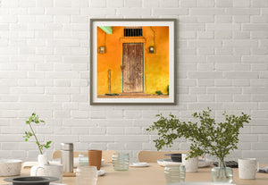 Square colour photograph of a rustic door beneath a barred opening in a bright Cuban facade.
