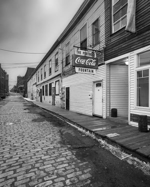 Weathered wharf buildings and projecting signs line a quiet Portland waterfront street.