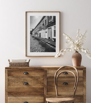 Vertical monochrome photograph of Custom House Wharf with textured paving and old shop fronts.