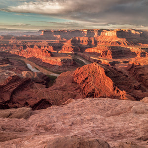 Sunlit sandstone cliffs and a rough foreground ledge overlook a winding river at Dead Horse Point.