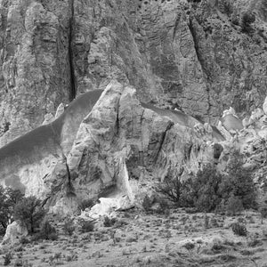 Rounded desert rock formations beneath a fractured cliff wall, monochrome photograph.