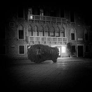 Black and white night photograph of the Eros Bendato sculpture and surrounding buildings.