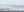 A wide Antarctic landscape of layered white snow, broken ice faces and dark sea.
