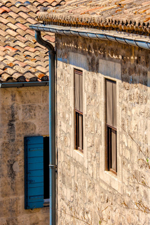 Colour photograph of French stone architecture with tiled roofs and a vivid blue shutter