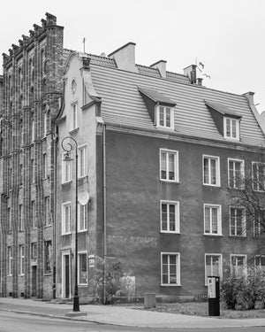 Vertical monochrome photograph of a tiled roof and dormer windows beside an ornate brick building in Gdańsk