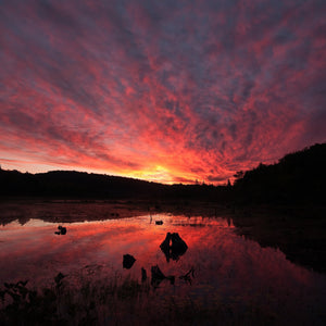 A fiery morning sky glows above wooded hills and still lake water