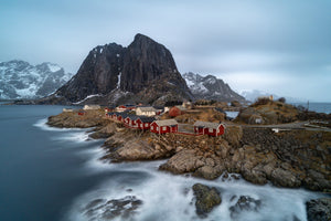 Soft blue water and white surf surround red fishing cabins on Norway’s coast