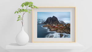 Red wooden cabins on stilts contrast with rugged rocks and pale winter sky