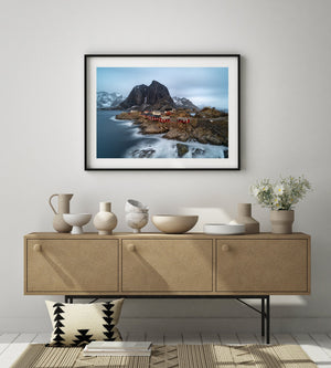 A quiet Norwegian shoreline combines red cottages, blue sea and steep winter mountains
