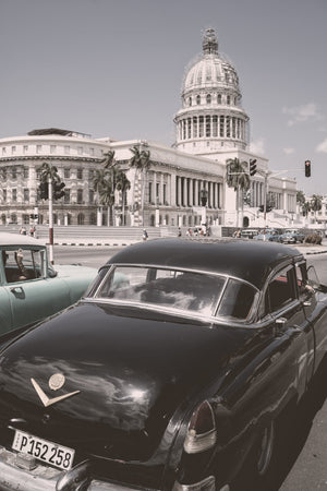 Rear view of a dark vintage car outside El Capitolio in Havana, Cuba.