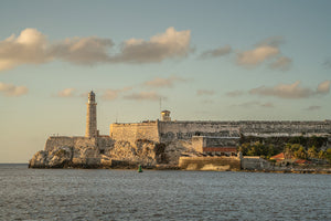 Stone lighthouse and fortress walls on Havana’s rocky coast beneath softly lit clouds.