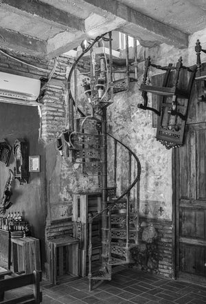 A narrow metal spiral stair rises beside peeling plaster and exposed brick in Havana.