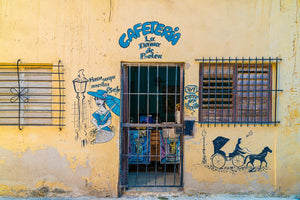 Colour photograph of a weathered yellow Havana facade with a woman mural and horse-drawn carriage illustration.
