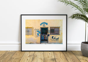Cafeteria La Dama de Belen sign above a barred doorway on a yellow Havana wall.
