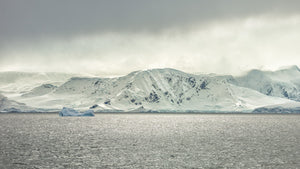 Snow-covered Antarctic mountain ridges stretching along the shore beyond gently rippling grey water.