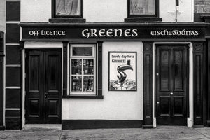 Irish pub facade with painted lettering, a display window and two dark entrances in monochrome.