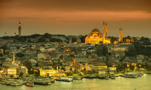 Warm evening lights glow across Istanbul’s skyline above a busy waterfront lined with ferries.