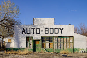 White auto body shop facade with green doors and boarded windows
