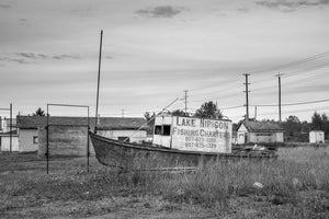 Weathered fishing boat with Lake Nipigon charter lettering beside old buildings.