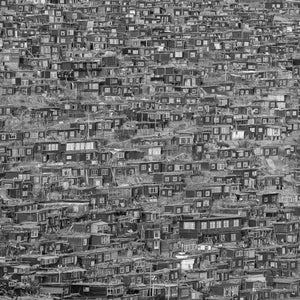 Monochrome photograph of wooden dwellings layered across a rocky slope in Larung Gar.