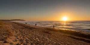 Sunrise walkers on a sandy Australian beach with light reflected across the surf