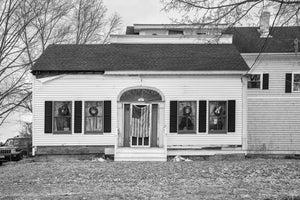 White clapboard Maine house with dark shutters and a flag-covered doorway