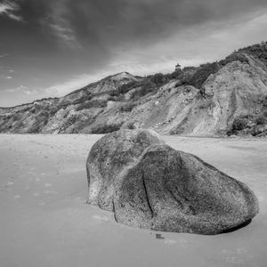 Rounded beach boulder below coastal cliffs and a distant lighthouse on Martha’s Vineyard