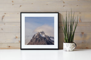 Dark layered rock and white snow rise beneath a pale blue sky