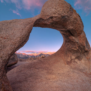 Rounded granite arch surrounds a view of distant mountain summits