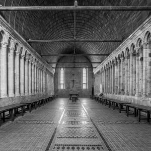 Symmetrical rows of narrow arches lead toward tall windows at the end of a stone hall