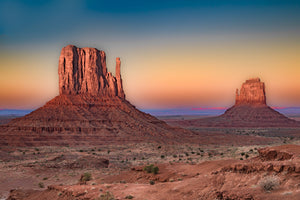 Two sandstone buttes rise above the desert in warm evening light
